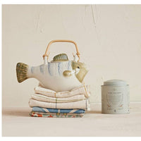 Showing  fish teapot on a stack of towels. 
A whimsical fish shapes tea pot made of stoneware and a bamboo handle is a fun, coastal touch.  Perfect for brewing and serving tea. Comes with  metal strainer 9.25” L x 5.25” W x 5.25” H