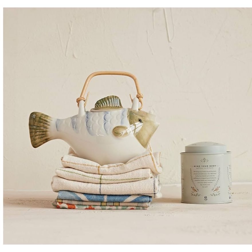 Showing  fish teapot on a stack of towels. 
A whimsical fish shapes tea pot made of stoneware and a bamboo handle is a fun, coastal touch.  Perfect for brewing and serving tea. Comes with  metal strainer 9.25” L x 5.25” W x 5.25” H