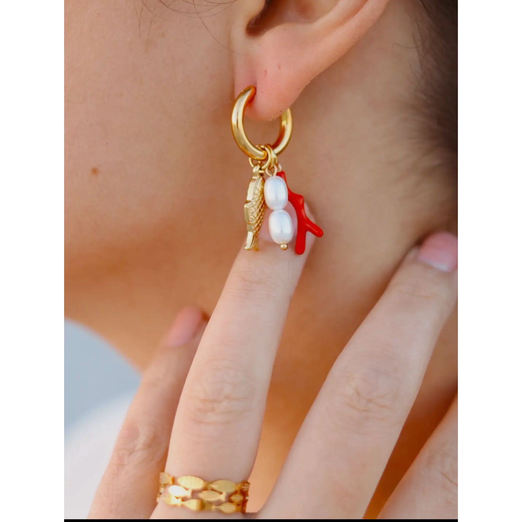 Gold plated hoop water proof fish shaped earrings with orange coral and pearls. Show in woman’s ear