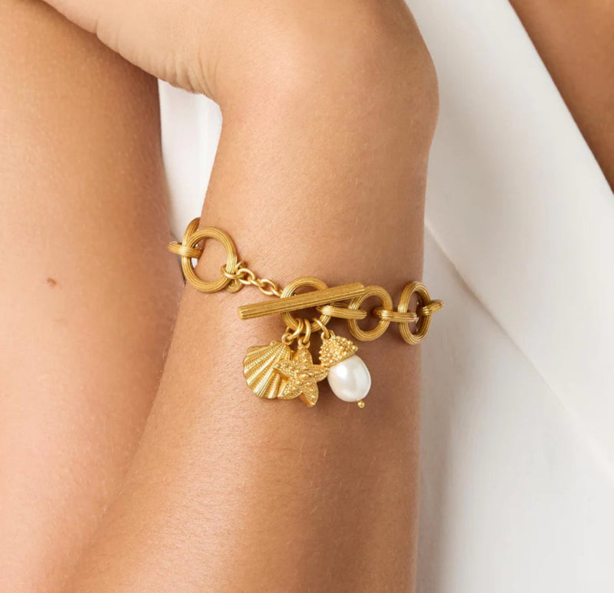 Gold bracelet with charms on a wrist against a white background
