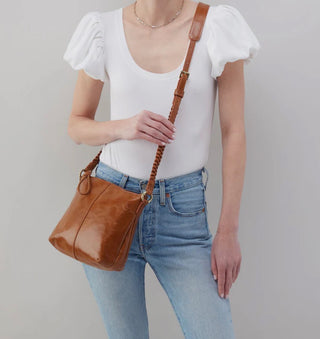 Person wearing a white top and blue jeans holding a brown leather bag against a plain background