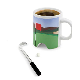 Showing the mug full of coffee and the golf ball and club ready to putt 