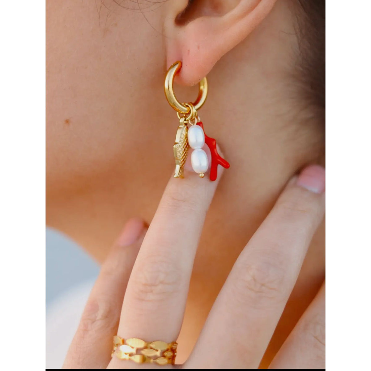 Gold plated hoop water proof fish shaped earrings with orange coral and pearls. Show in woman’s ear 