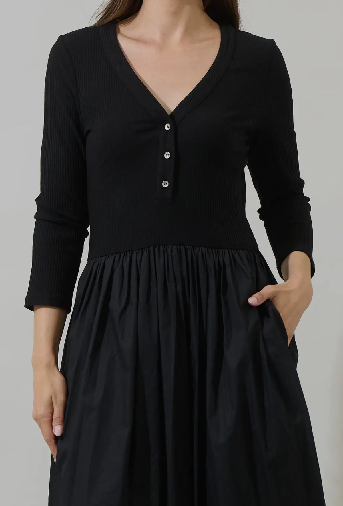 Make an effortless statement in this ultra flattering, versatile dress. It features a rib knit bodice and flared, gathered skirt for a beautifully balanced silhouette, finished with long sleeves, a split neckline, and button detail. A dropped waist and functional pockets add comfort and ease. Style with boots and a crossbody or dress it up with heels and bold accessories.

- Midi
- Long sleeves
- Knit
- Pockets
- Color: Black

Size + Fit
- Model is 5'9" and wearing size XS
- Measurements taken from size S
-